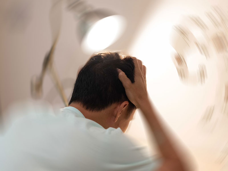 man holding head with surrounding room spinning