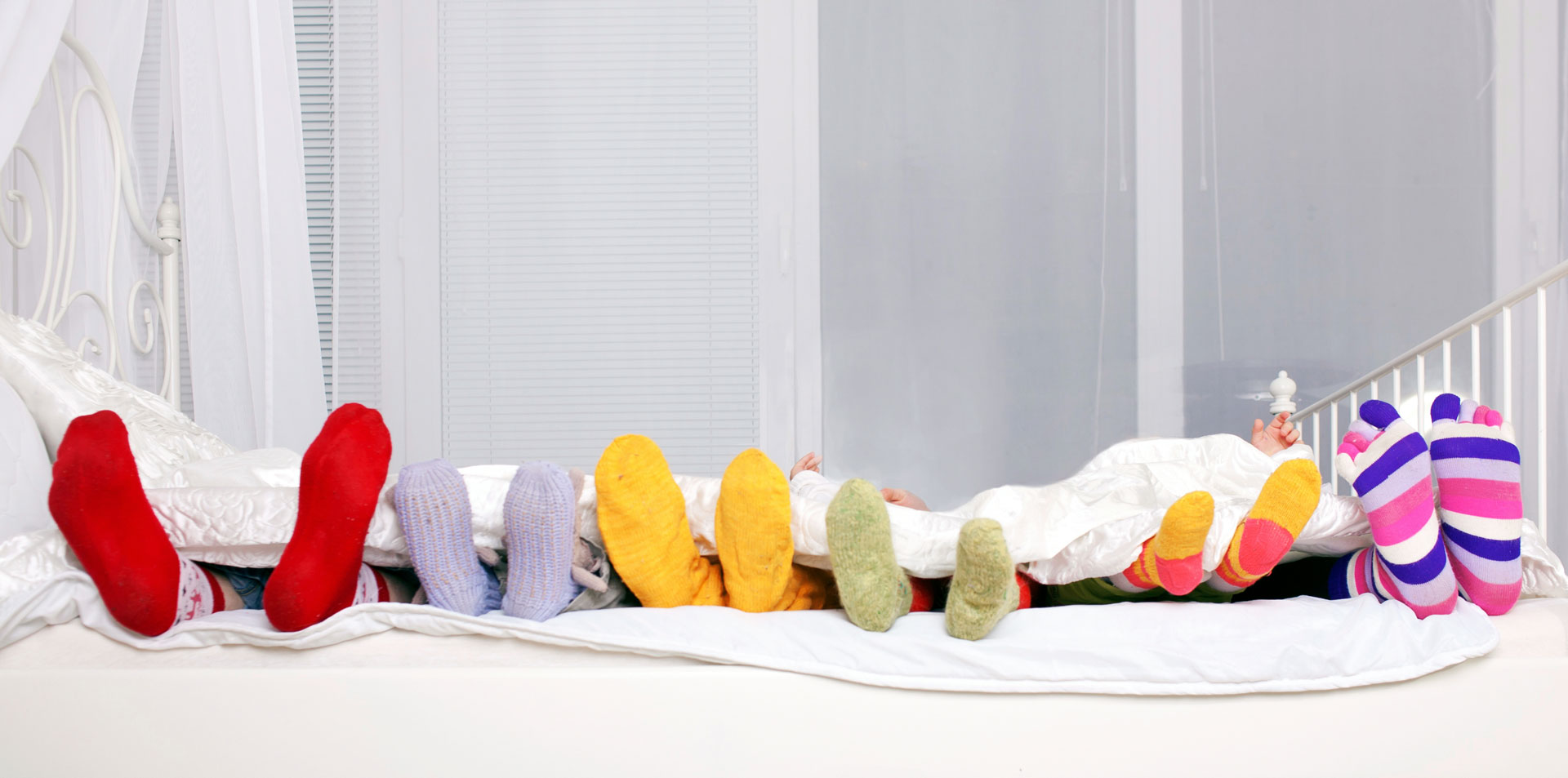 Feet of father, mother and four children in colorful knitted socks on white bed