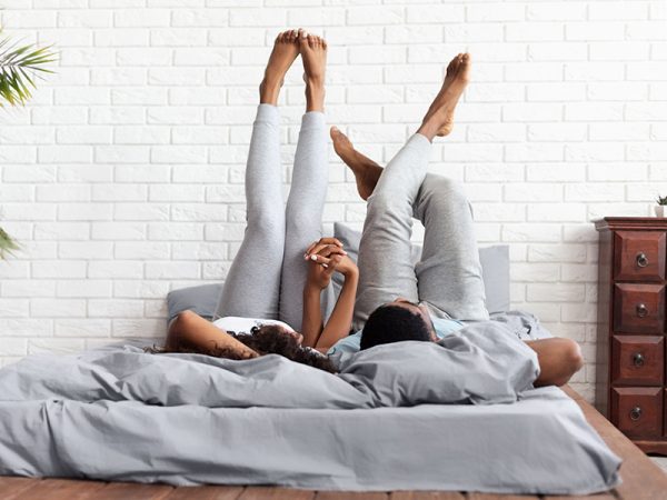Happy couple lying on bed at home raising legs up
