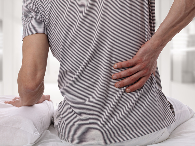Man suffering from back pain at home in the bedroom