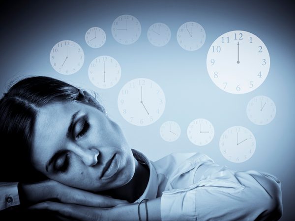 Tired young woman in white is sleeping. Sleep and Time concept. Clocks as background