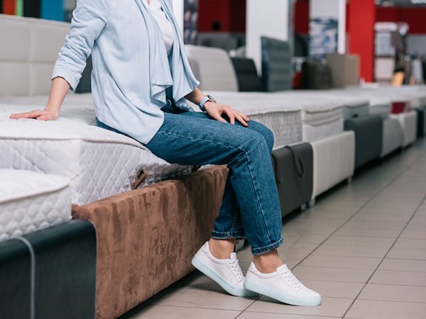 partial view of woman sitting on mattress in furniture shop