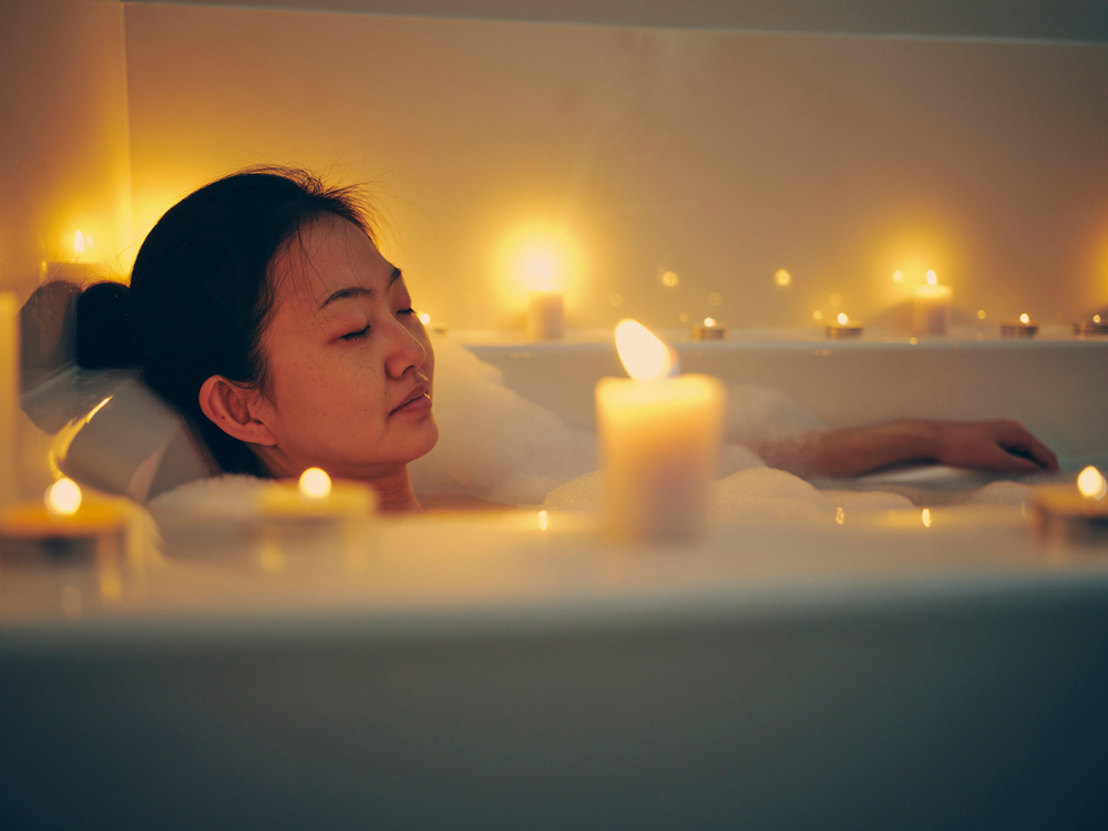 woman relaxing in a bathtub, surrounded by candles.