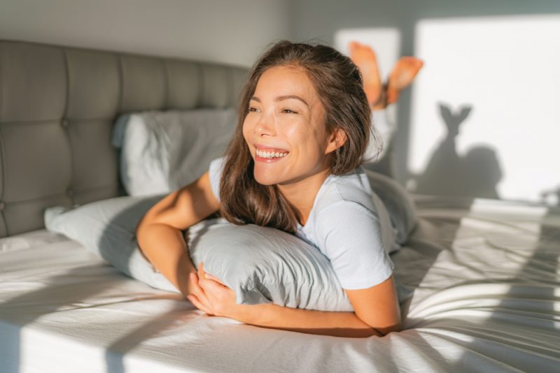 woman waking up early morning happy enjoying sun on comfortable mattress and pillow