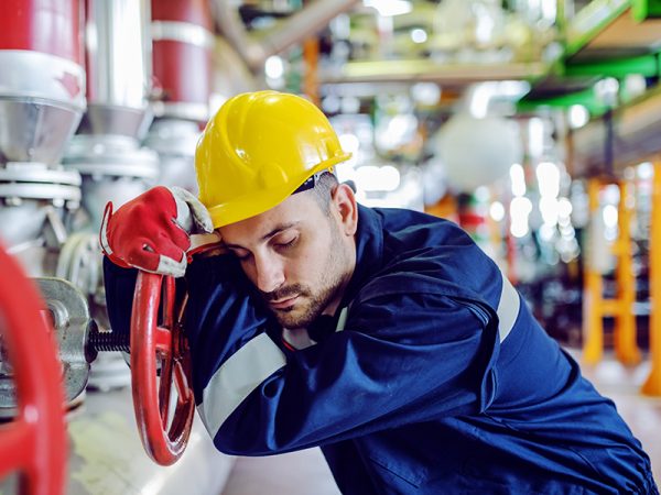 Hardworking caucasian worker in working clothes leaning on big valve and sleeping