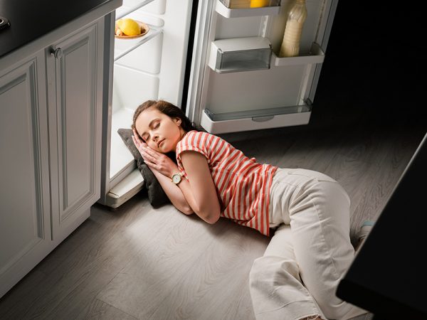 High angle view of attractive girl sleeping on pillow near open refrigerator